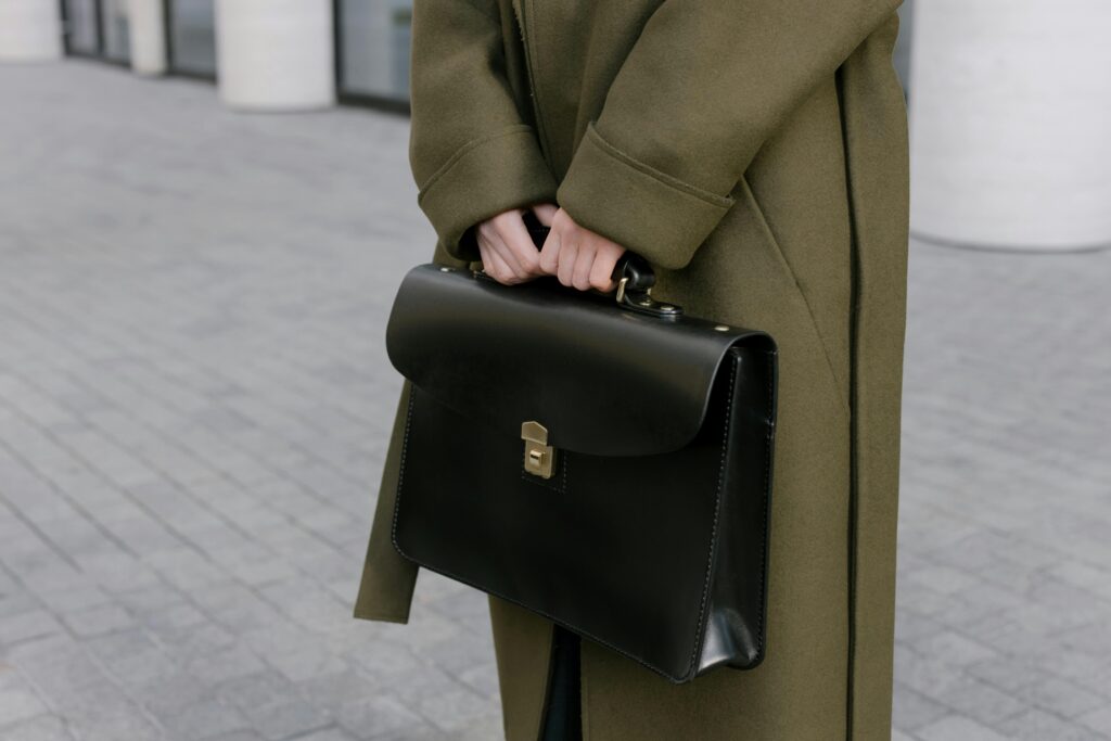 Close-up of a woman in a coat holding a black briefcase on a paved street.