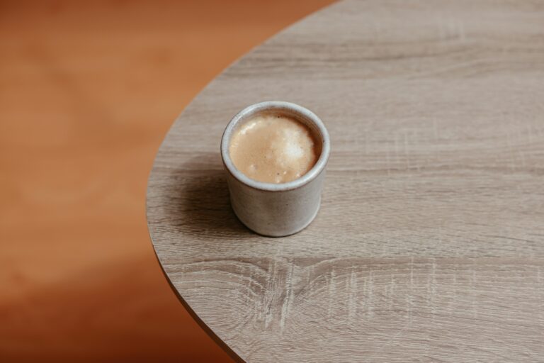 A rustic coffee cup filled with hot beverage on a simple wooden table, viewed from above.