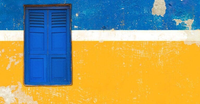 Bright blue shuttered window on a blue and yellow textured wall, showcasing vibrant colors.