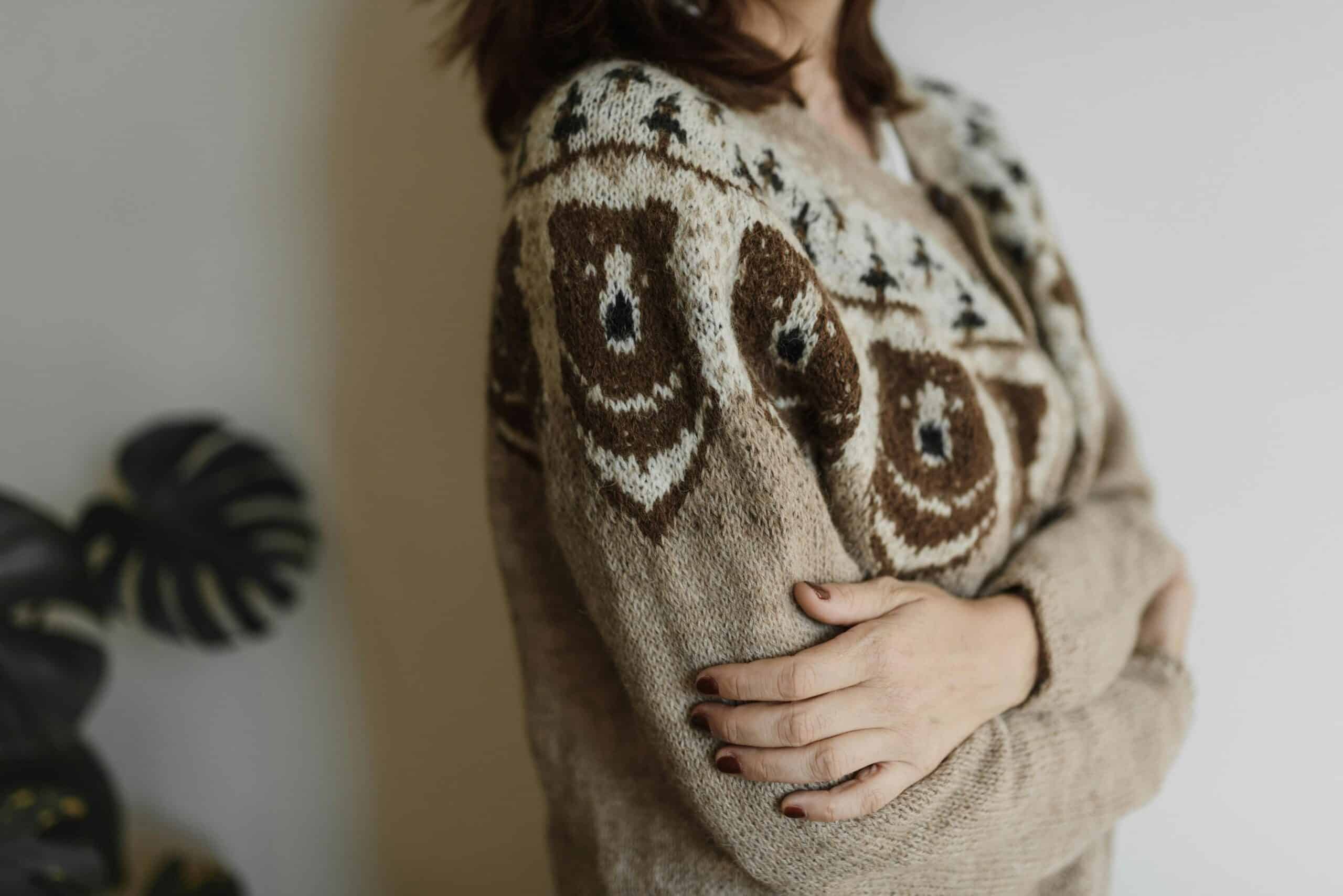 Close-up of a person wearing a cozy bear-design knitted sweater indoors.