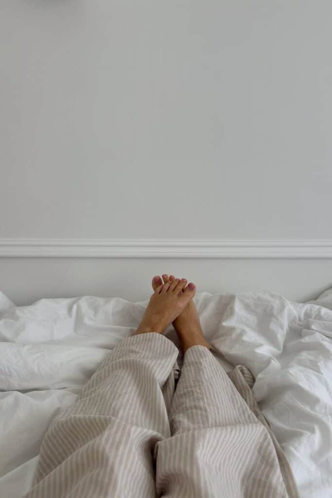 Relaxing morning in bed with legs covered in pajamas on white sheets. Tranquil indoor setting.
