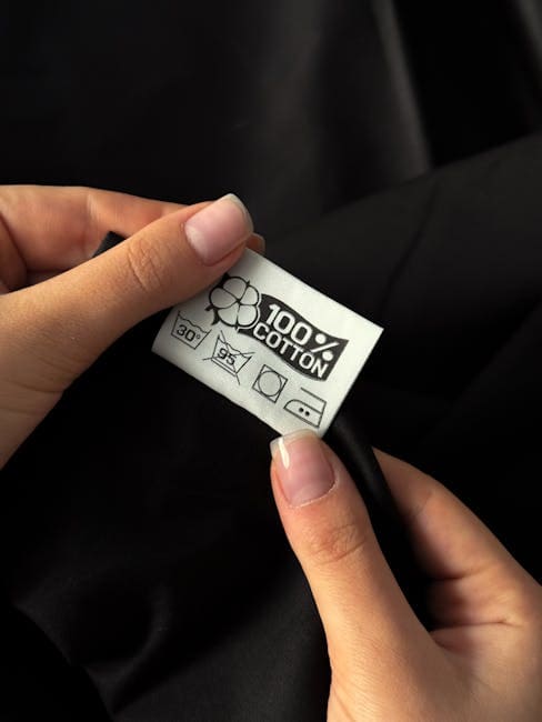 Hands of a woman examining a 100% cotton tag on clothing against a dark background.
