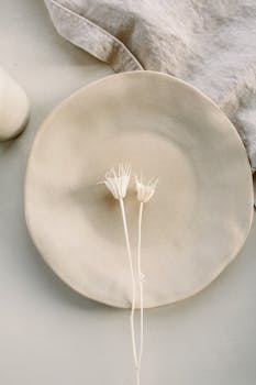Elegant minimalist composition of a ceramic plate adorned with delicate white flowers on a linen cloth.