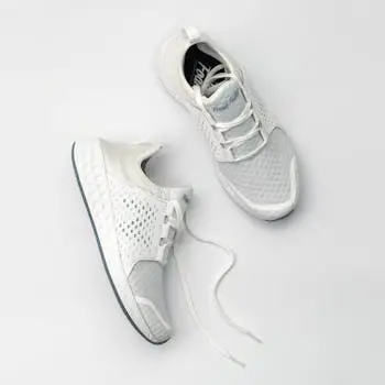 Pair of modern white sneakers with laces on a neutral backdrop.