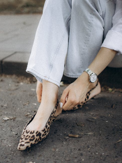 Close-up of a woman adjusting her leopard print flat shoes while seated on the pavement.
