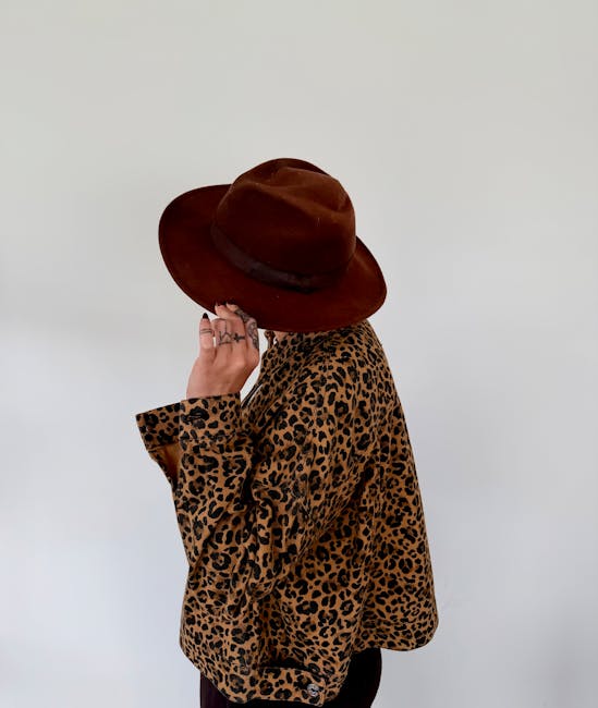 Woman wearing leopard print jacket with brown hat on white background.